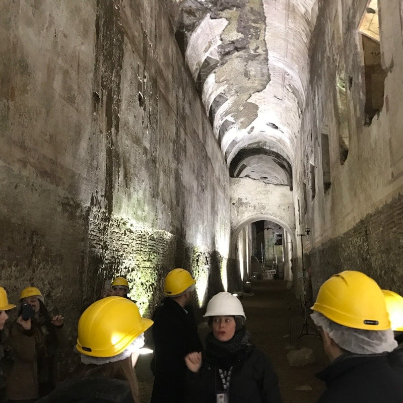 A group of tourists wearing helmets and preparing to tour a vast vaulted corridor in the Domus Aurea in Rome.