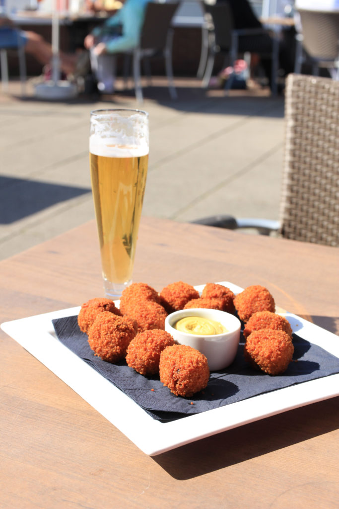 Glass of beer next to a plate of Dutch beiterballen at a sidewalk cafe in Amsterdam
