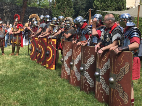 A row of people dressed as Roman Centurions holding shields and wearing helmets.