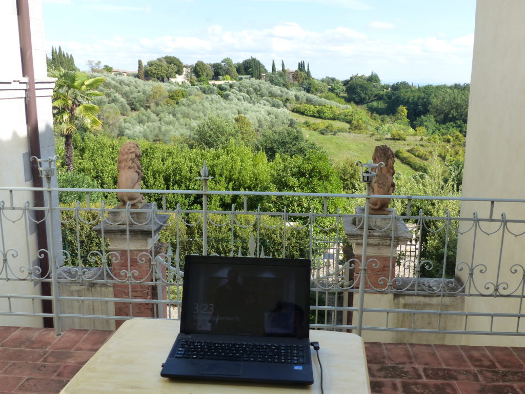 View of the Tuscan countryside from a balcony with a laptop in front