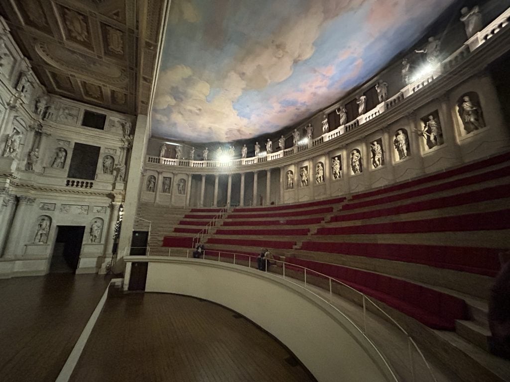 The audience seating area at the Teatro Olimpico in Vicenza, featuring red-upholstered benches and a painted sky ceiling. A must-see near Padua for theater and architecture enthusiasts.