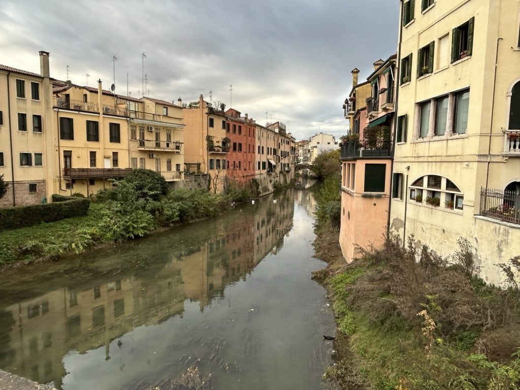 A peaceful canal in Padua lined with colorful historic buildings and lush greenery, perfect for a scenic walk or boat ride. A must-see spot while exploring Padua.