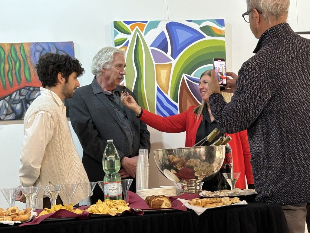 A lively art opening near Padua, featuring artist Gregg Simpson, guests, and vibrant modern paintings in the background. A cultural highlight for art enthusiasts visiting the area.