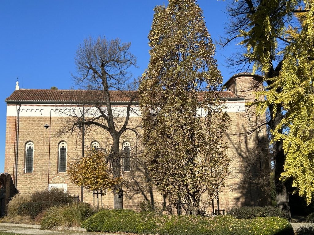  The exterior of the Scrovegni Chapel in Padua, surrounded by lush greenery and clear blue skies. An iconic landmark and a treasure trove of Renaissance art.