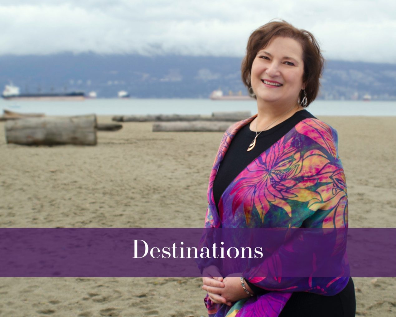 A woman standing on a sandy beach, wrapped in a colorful shawl, with a cloudy sky and logs in the background. The overlay text reads "Destinations."