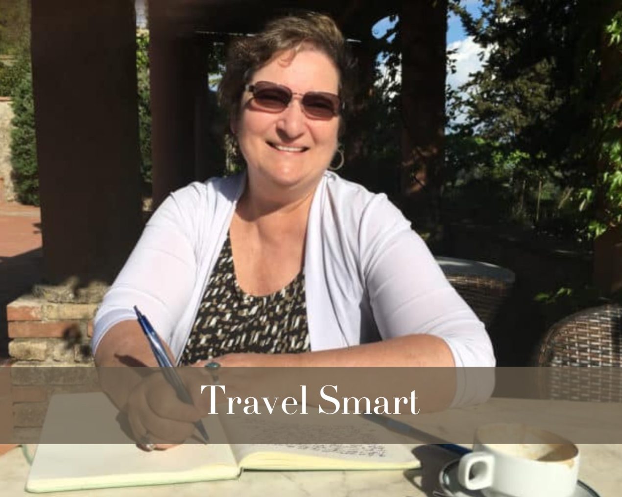 A woman sits at a sunny outdoor café, writing in a notebook. The overlay text reads "Travel Smart."