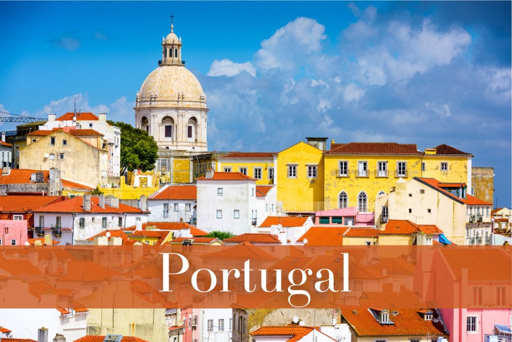 The historic Alfama district in Lisbon, Portugal, with yellow and white buildings, red-tiled rooftops, and the imposing dome of the National Pantheon standing against a bright blue sky with fluffy clouds.