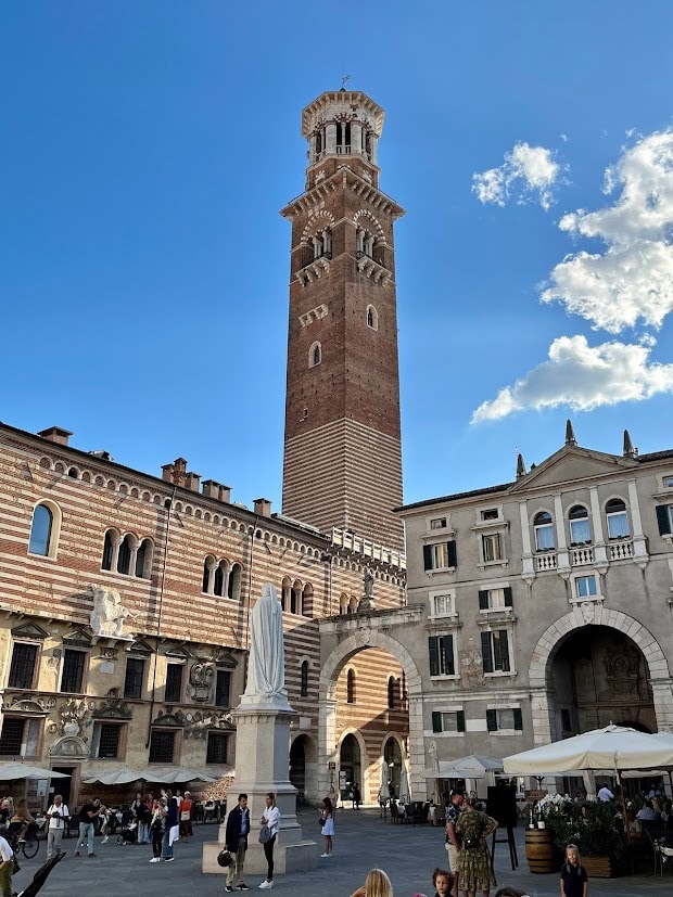 A side view of Palazzo della Ragione, with striped stone walls and a tall clock tower, located in Verona’s historic center.