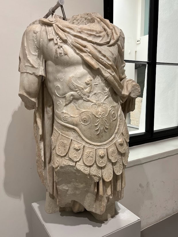 A marble sculpture of a Roman soldier’s torso, featuring intricate armor details including a lion motif and decorative medallions.