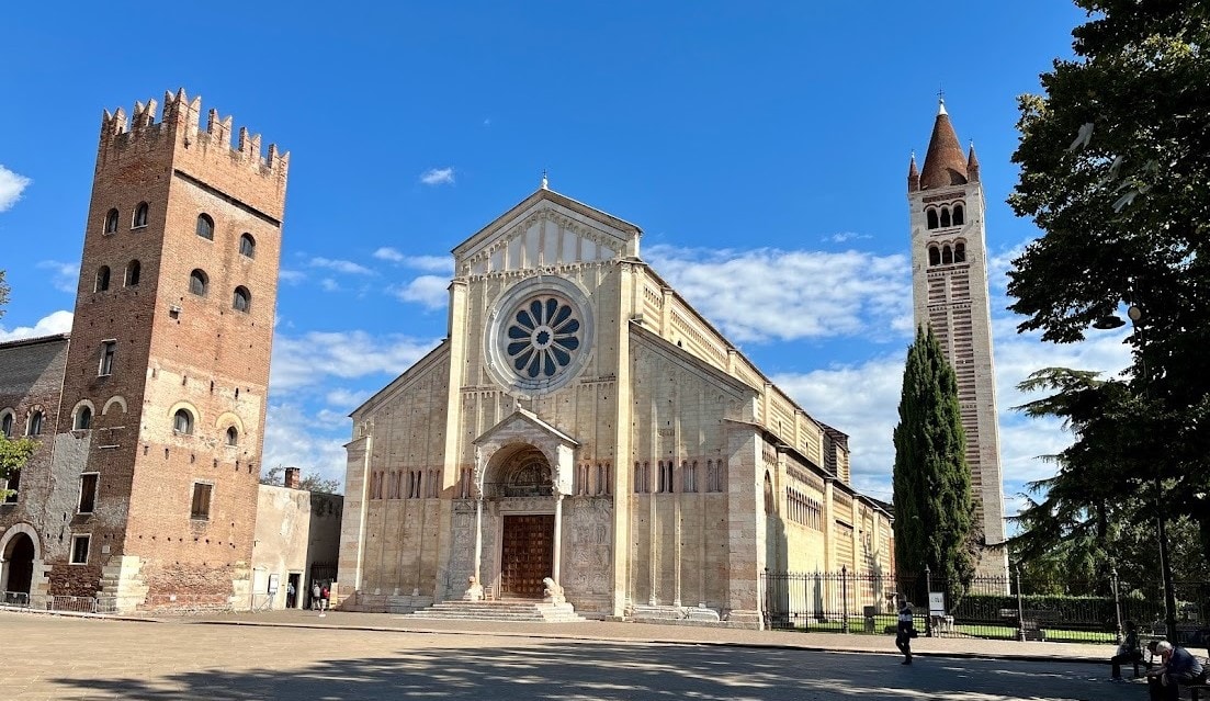 The exterior of the Basilica of San Zeno, featuring a Romanesque design with a rose window, stone facade, and two nearby towers.