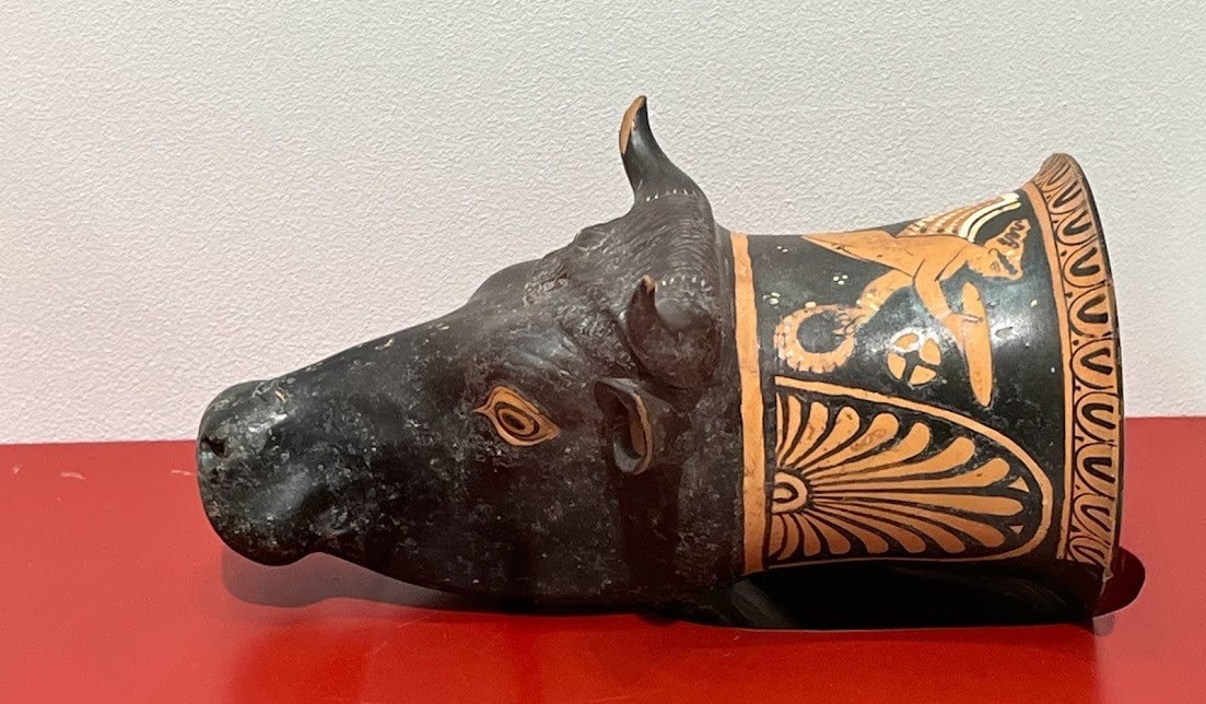 A ceramic rhyton in the shape of a bull’s head, adorned with black and orange decorative patterns and motifs.