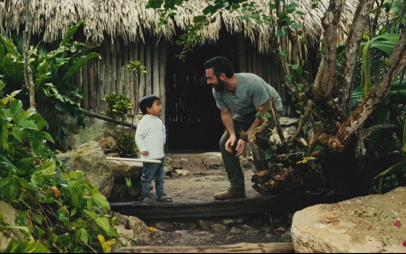 Documentary filmmaker Brady Skye is talking with a small Maya boy in front of a grass hut in the Yucatan area of Mexico